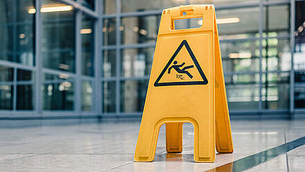 RENOLIT_gelbes Schild auf dem Boden, das vor nassem Boden warnt