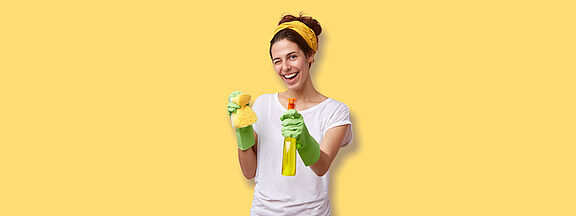 Frau vor einem gelben Hintergrund mit einem Schwamm und einer Sprühflasche in der Hand